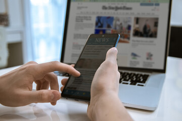Man reading news online on a smartphone and laptop. Reads articles, newspaper, information concept