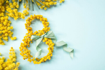 Obraz premium International Women's Day. A banner, a flyer, a beautiful postcard for March 8th. Yellow mimosa flowers in the shape of the number eight and a ribbon bow on a turquoise, blue background.
