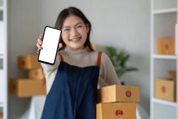 Beautiful smiling Asian woman holding a cardboard box and hands showing a smartphone mockup of a...