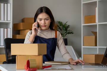 Young Asian business woman online seller talking confirming orders from customer on phone in home office. Logistics, Packages ready for shipment. Selling products online. Concept of shopping online