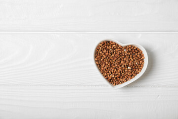 Raw buckwheat in a bowl on a textured wooden background. Wheat grains, porridge, cereals, raw buckwheat in a plate. Healthy food. Porridge. Diet. Organic cerea. Space for text.Copy space.