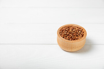 Raw buckwheat in a bowl on a textured wooden background. Wheat grains, porridge, cereals, raw buckwheat in a plate. Healthy food. Porridge. Diet. Organic cerea. Space for text.Copy space.