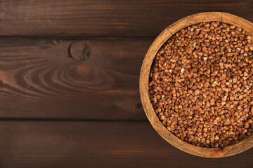 Raw buckwheat in a bowl on a textured wooden background. Wheat grains, porridge, cereals, raw buckwheat in a plate. Healthy food. Porridge. Diet. Organic cerea. Space for text.Copy space.