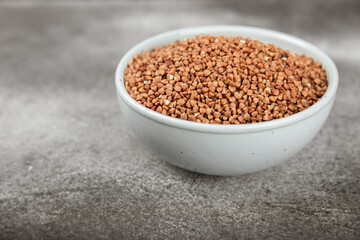 Raw buckwheat in a bowl on a textured wooden background. Wheat grains, porridge, cereals, raw buckwheat in a plate. Healthy food. Porridge. Diet. Organic cerea. Space for text.Copy space.