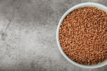 Raw buckwheat in a bowl on a textured wooden background. Wheat grains, porridge, cereals, raw buckwheat in a plate. Healthy food. Porridge. Diet. Organic cerea. Space for text.Copy space.