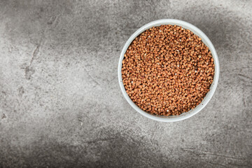 Raw buckwheat in a bowl on a textured wooden background. Wheat grains, porridge, cereals, raw buckwheat in a plate. Healthy food. Porridge. Diet. Organic cerea. Space for text.Copy space.