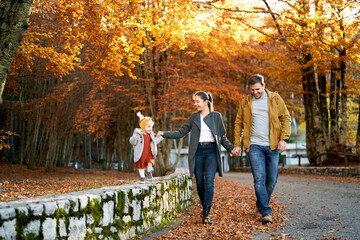 Dad, mom and a little girl walk holding hands in the autumn park
