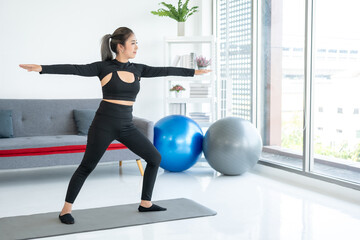Obraz premium Beautiful smiling Female wearing sportswear exercise training yoga in living room. Attractive asian young fitness woman stretching warming up before workout at home.
