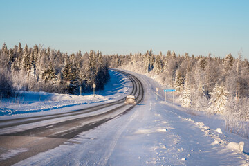 Fototapeta na wymiar Frosty sunny winter snow-covered highway through hills covered with snowy coniferous forest.
