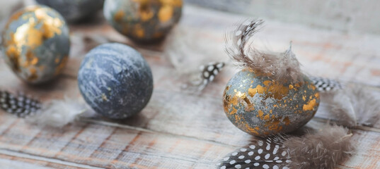 Happy Easter 2024. Stylish grey Easter eggs in the color of marble, concrete, gold and beautiful feathers on a wooden background. Egg coloring with natural dye karkade tea. 