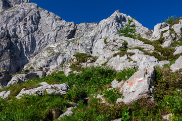 Path mark inidcating hiking trail from Fusine Lake to Mangart saddle in Tarvisio, Julian Alps, Friuli Venezia Giulia, Italy, Europe. Rugged mountain rock formations on extreme alpine terrain in summer - obrazy, fototapety, plakaty