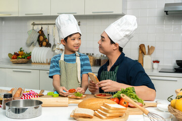 Happy moment asian father and son cooking breakfast in the kitchen. Dad and child asian family having fun preparing food bread egg sandwich. Positive parent and kid nice relationship