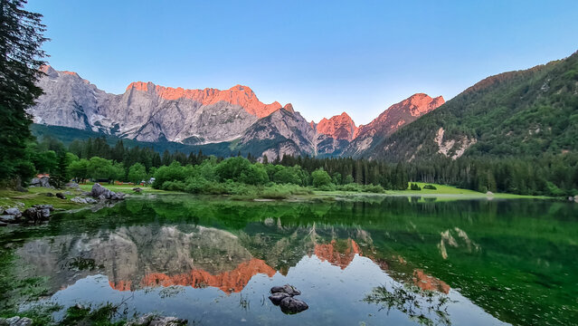 Morning sunrise view of Superior Fusine Lake (Laghi di Fusine) with majestic Mount Mangart in background in Tarvisio, Friuli Venezia Giulia, Italy. Captivating Water Reflection in tranquil atmosphere