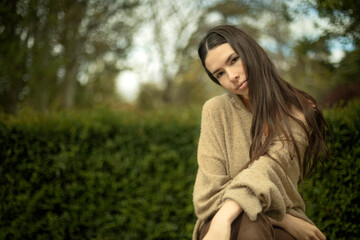 Outdoor portrait of young caucasian model woman sitting looking serious with out of focus plant...