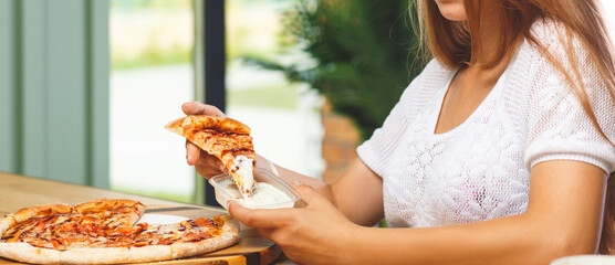 A girl dips a slice of pizza in sauce
