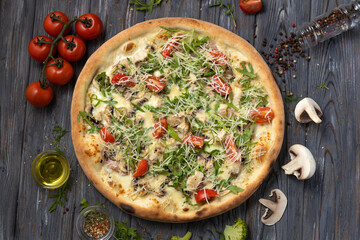 Delicious pizza with chicken breast, cherry tomatoes, arugula,mushroom and parmesan on a wooden background.Top view