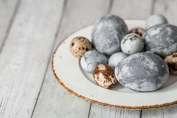 Stylish grey Easter eggs in the color of marble, concrete in a plate and willow branches on a white...