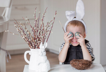 Portrait of a little boy with bunny ears on his head and Easter eggs in his hands. Preparing the...