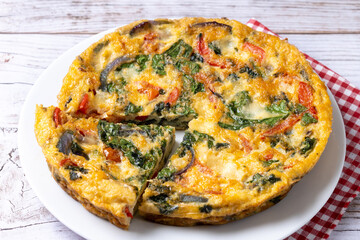 Italian Frittata made with spinach, tomatoes, onion and peppers on white wooden table