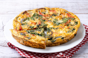 Italian Frittata made with spinach, tomatoes, onion and peppers on white wooden table