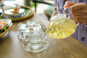 Woman is pouring jasmine tea from glass kettle into a cup