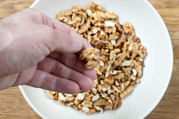 a piece of walnut in a hand on the background of a plate with nuts