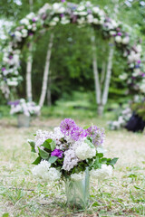 A bouquet of lilac flowers, purple giant onions, and other flowers in a small bucket as a decorative element against the background of a wedding arch. Vertical orientation - 706327825
