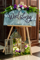Wooden invitation sign in the shape of a tripod, decorated with flowers and the word 