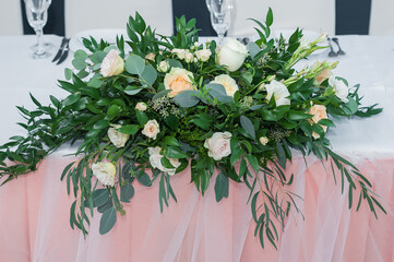 Flower arrangement stands on a wedding table. Beautiful floral composition consists of different types of roses, eucalyptus, and other plants.