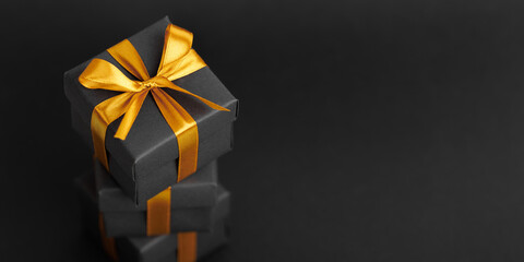 Black gift box with golden ribbon bow on black background