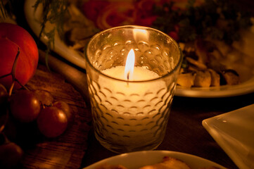 Burning wax candle in a small glass cup on a dinner table. - 706331266