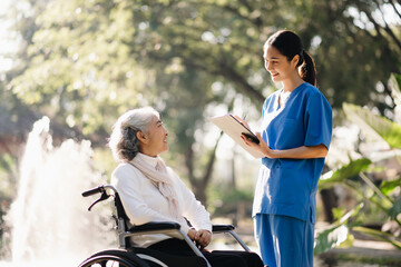 Elderly asian senior woman on wheelchair with Asian careful caregiver and encourage patient, walking in garden. with care from a caregiver. and senior health insurance