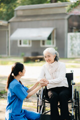 Fototapeta premium Elderly asian senior woman on wheelchair with Asian careful caregiver and encourage patient, walking in garden. with care from a caregiver. and senior health insurance