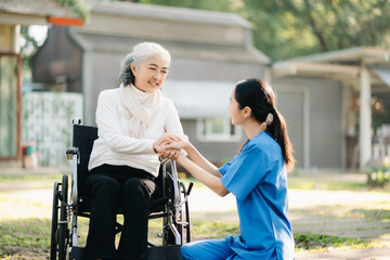 Fototapeta na wymiar Elderly asian senior woman on wheelchair with Asian careful caregiver and encourage patient, walking in garden. with care from a caregiver. and senior health insurance