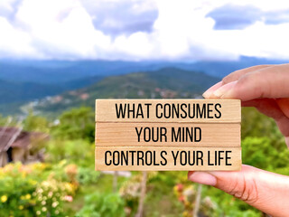 Motivational inspirational quote. What consumes your mind, controls your life on wooden blocks with nature background.