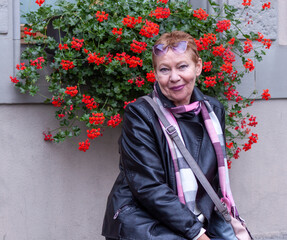 Smiling lady of mature age against the background of a bush with red flowers