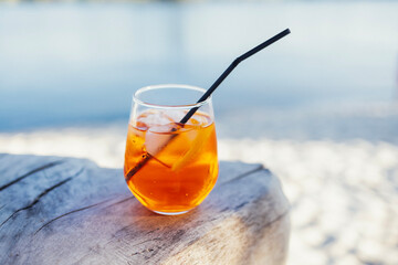 Orange slice and aperol spritz cocktail on a stone against the backdrop of a sandy beach