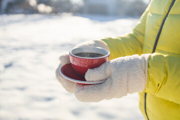 Woman in woolen gloves holds a red cup of coffee in the winter city outdoors. Hot and warming drinks in the winter concept. Hands close up. High quality photo