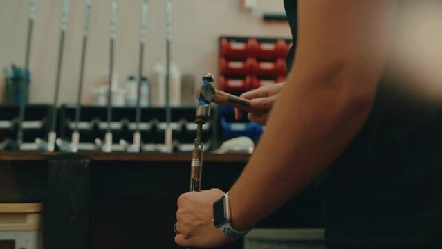 Male hands hammer nail into golf club shaft for custom fitting in workshop in slow motion