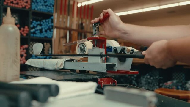 Golf club builder locking in club shaft on gripping vice and pulling sticky tape in slow motion