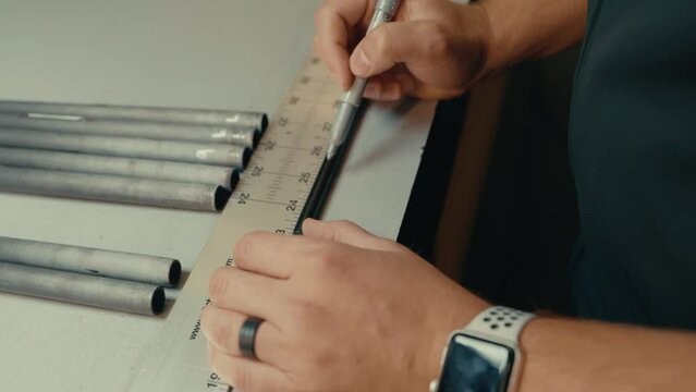 Male hands use ruler and pen to measure golf club shaft length for custom fitting on workshop counter in slow motion