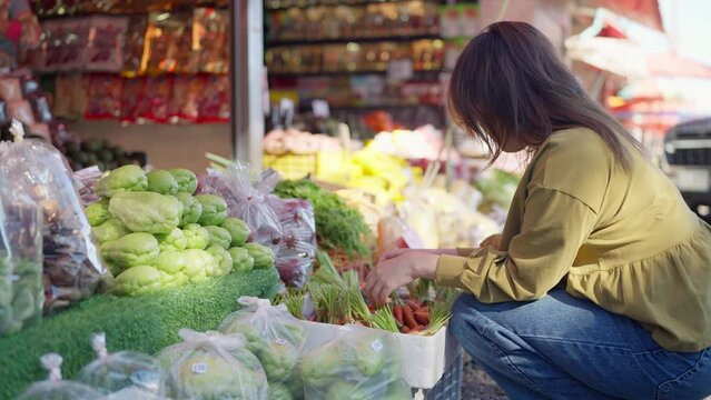 Young asian woman tourist choosing baby carrot at the local market. Healthy woman choosing fresh vegetables in the market. Vegetables and fruits concept