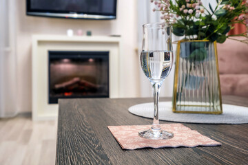 glass of sparkling wine or champagne on table with bouquet of flowers in front of fireplace