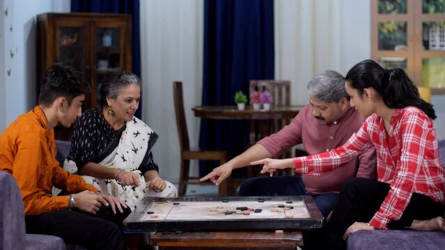 An aged Indian couple playing carrom with their kids - board game  indoor game  happy family  small nuclear family. Grandchildren having fun with their grandparents - leisure activity  three genera...
