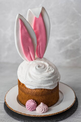 Beautiful stylish still life. Easter cake with rabbit (hare) ears, meringue, marshmallows, Easter eggs and willow branches and on a light concrete background. Happy Easter 2024.