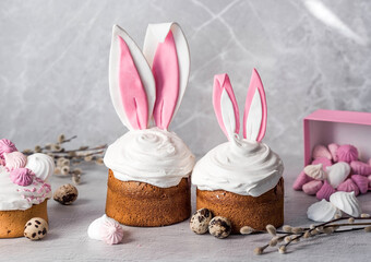 Beautiful stylish still life. Easter cake with rabbit (hare) ears, meringue, marshmallows, Easter eggs and willow branches and on a light concrete background. Happy Easter 2024.
