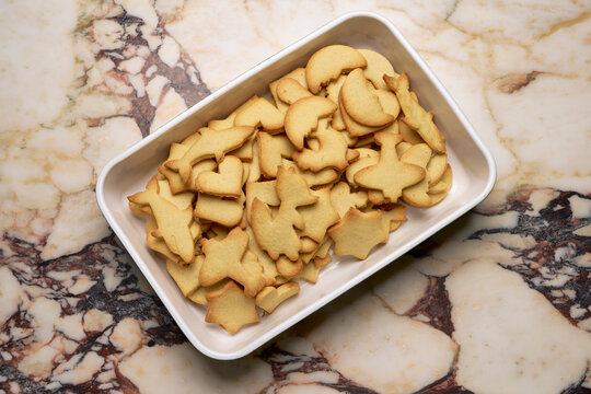 View from above sugar cookies in variety of shapes in dish on marble counter

