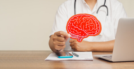 Brain health and dementia. Doctor holds a red brain symbol while sitting at a desk in the hospital.