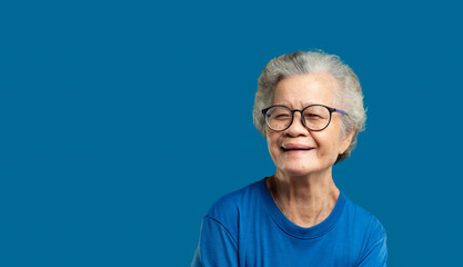 Portrait of an elderly Asian woman looking at the camera with a smile while standing on a blue...