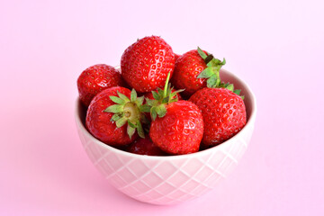 red strawberries in bowl isolated on pink background 
